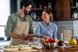 Beautiful young happy couple is using a digital tablet and smiling while cooking in kitchen at home