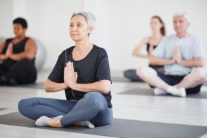 Healthy mature woman sitting on exercise mat in lotus position and doing yoga in the class