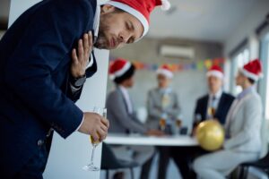 Sick businessman holding his chest in pain and coughing while being on New Year's party in the office.