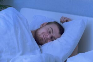 A bearded young man is night sleeping in a cozy bed. Happy to sleep. Healthy night sleep of a man in a fresh white bed.