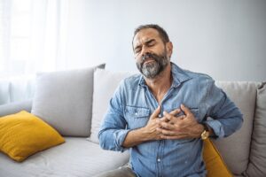 Closeup shot of a mature man holding his chest in discomfort at home. Shot of a handsome mature businessman holding his chest in pain while relaxing on a sofa at home
