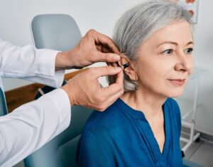 Senior woman during installation hearing aid into her ear by her audiologist, close-up. Hearing treatment for hearing impaired people
