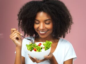 Studio shot of an attractive young woman eating salad against a pink background