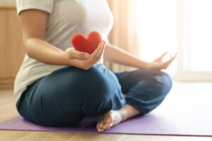Woman hold red yarn heart shape in hand doing yoga post at home. Yoga is good for heart - meditation concept.