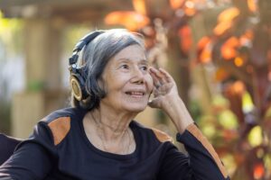 Asian senior woman listening music with headphone in backyard.