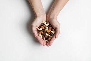 Cropped shot of woman's hands holding a pile of mixed nuts and dried berries over isolated white background. Healthy high-calorie vegan food concept. Close up, copy space, top view, flat lay.