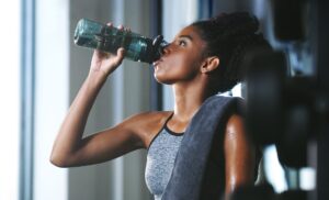 Shot of a sporty young woman drinking water while exercising at the gym