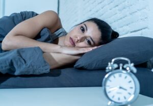 Sleepless and desperate beautiful latin woman awake at night not able to sleep looking at clock suffering from insomnia in sleep disorder concept.