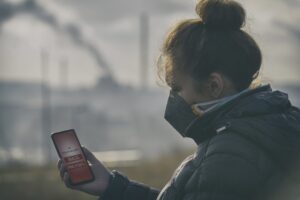 Woman wearing a real anti-pollution, anti-smog and viruses face mask and checking current air pollution with smart phone app